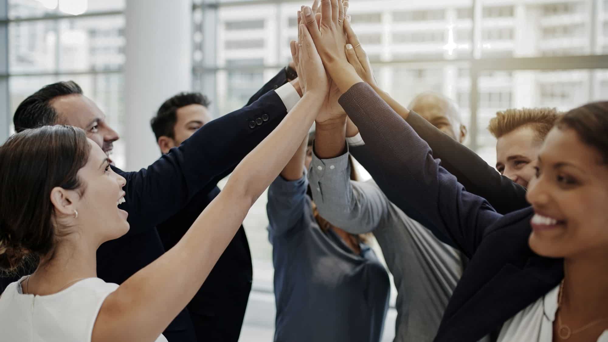 A group of diverse professionals in a modern office environment celebrating teamwork with a collective high-five, symbolizing effective employee motivation and collaboration.