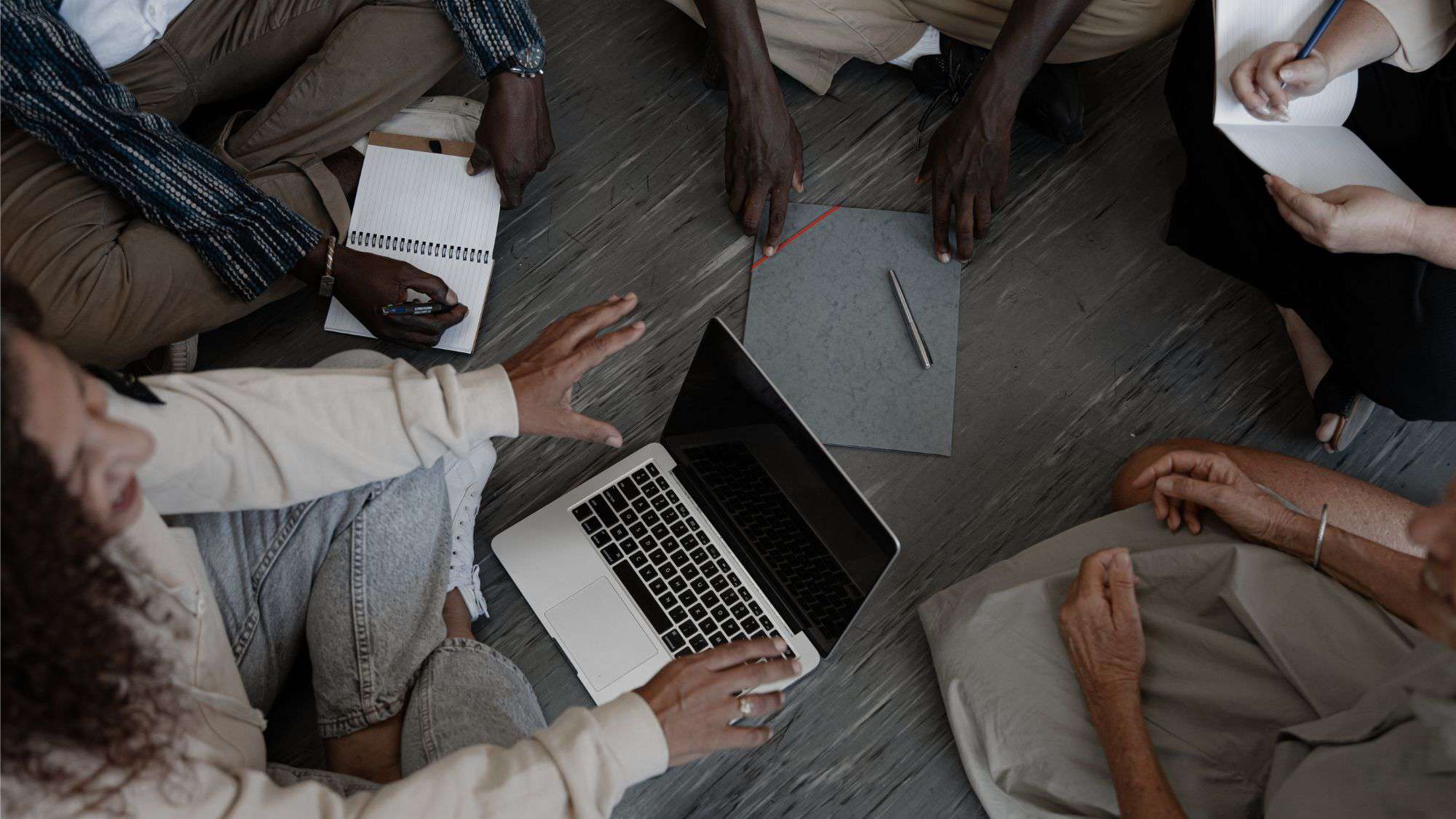 A diverse group of individuals sitting in a circle on the floor, collaborating with a laptop and notepads, symbolizing teamwork and strategic planning for nonprofit social media marketing.