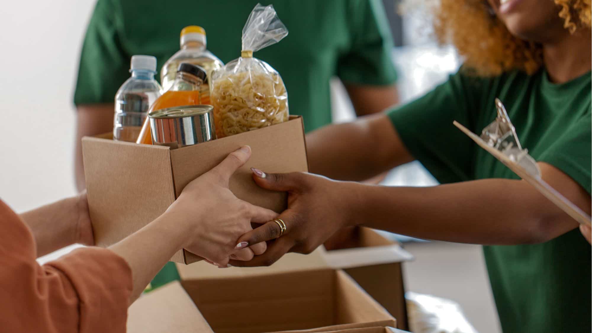 Volunteers handing over a box of donated food items, symbolizing the importance of choosing the right software for nonprofit organizations.